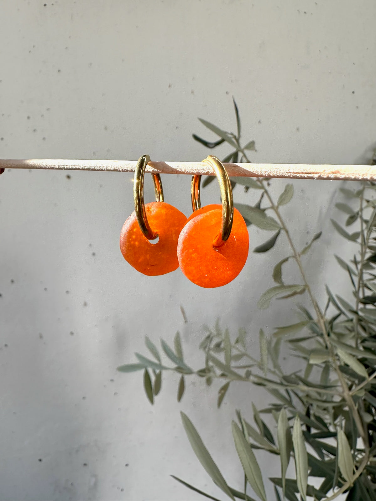 Argolas de aço com vidro reciclado, com vidro laranja, penduradas num ramo de oliveira