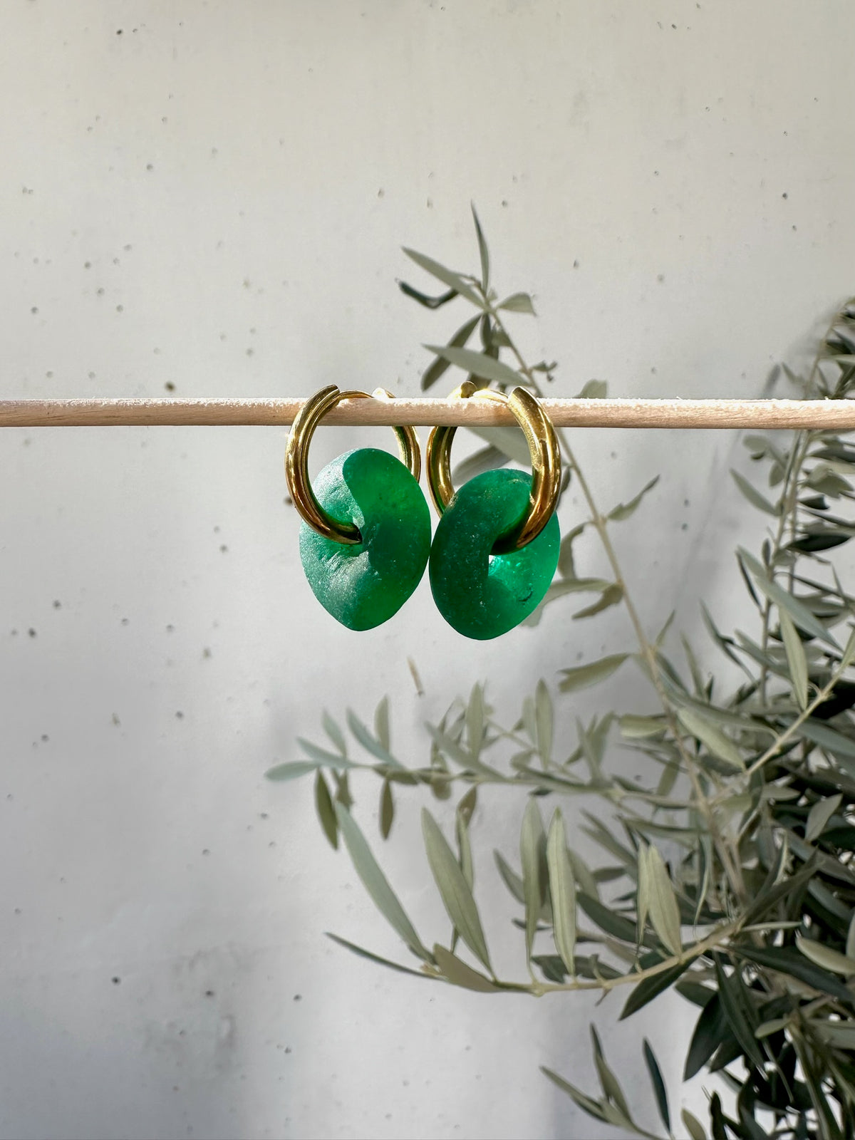 Argolas de aço com vidro reciclado, com vidro verde, penduradas num ramo de oliveira