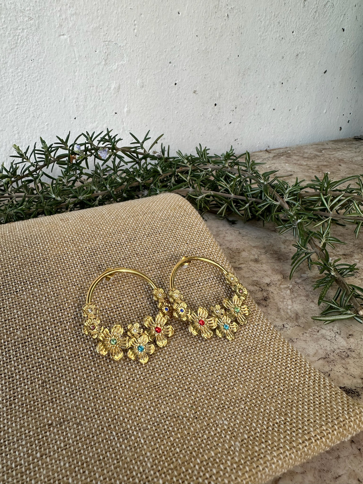 Brincos Aro de Flores de aço com banho de ouro, sobre tecido, com ramos verdes