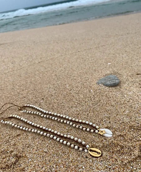 Colar Bacio di Mare de howlite com concha, pousado na areia da praia