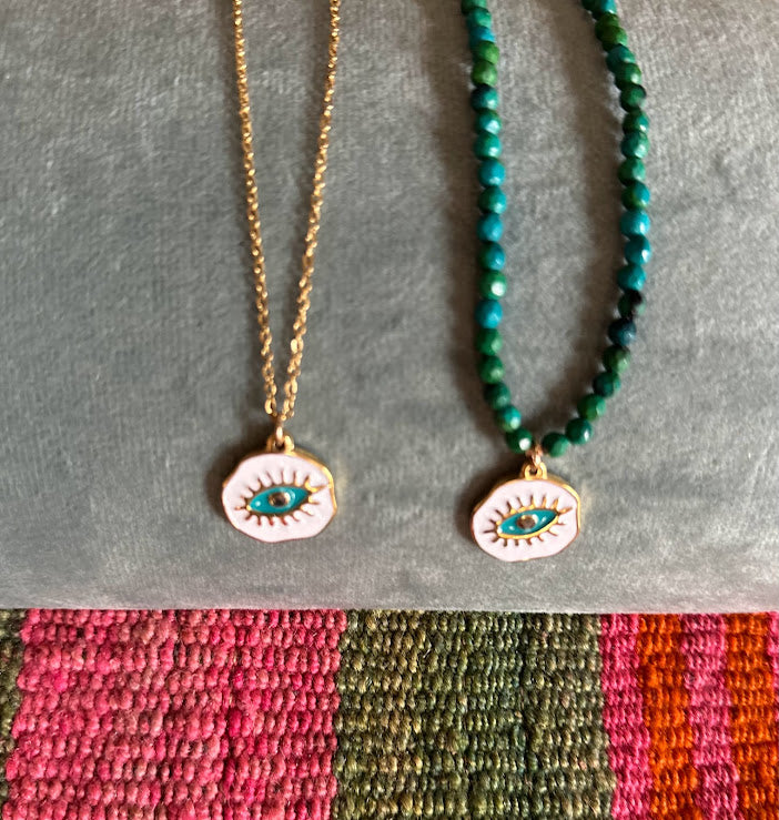 Colar Blueyes com medalha de aço esmaltada, em fio de aço e em pedras verdes, sobre tecido colorido