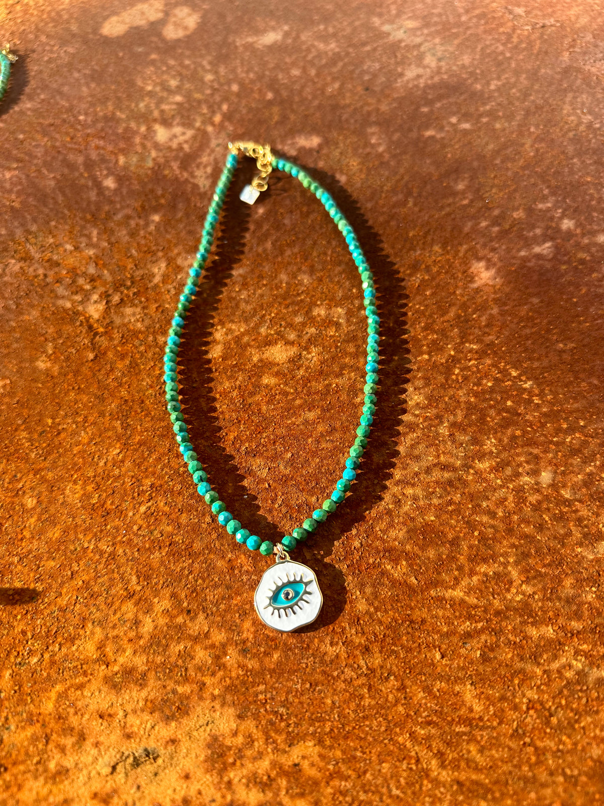 Colar Blueyes com medalha de aço esmaltada, em pedras verdes, sobre fundo cor de ferrugem