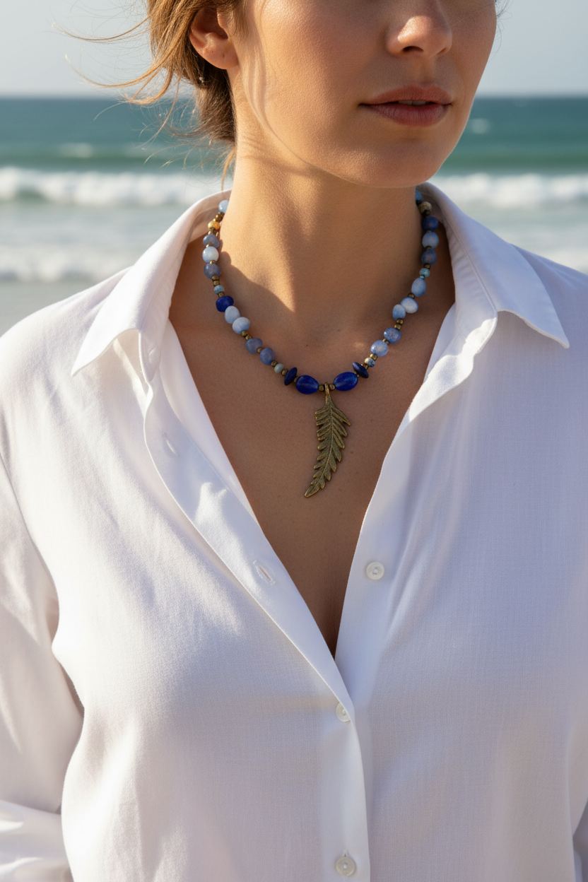Colar Boémia de ágata azul e bronze, com pendente de pena, usado por modelo junto ao mar