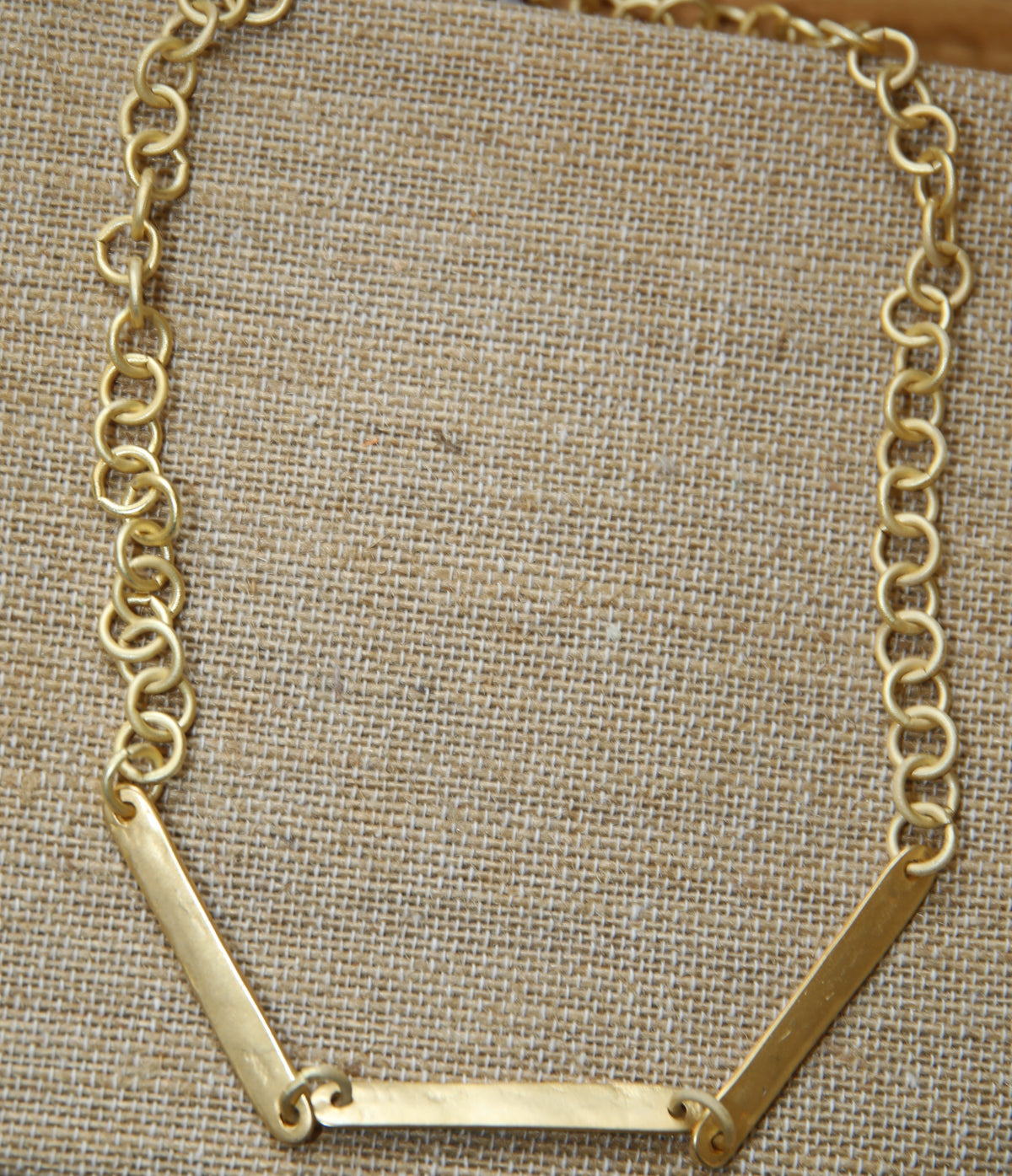 Colar Choker de corrente dourada, com barras douradas, sobre tecido de linho