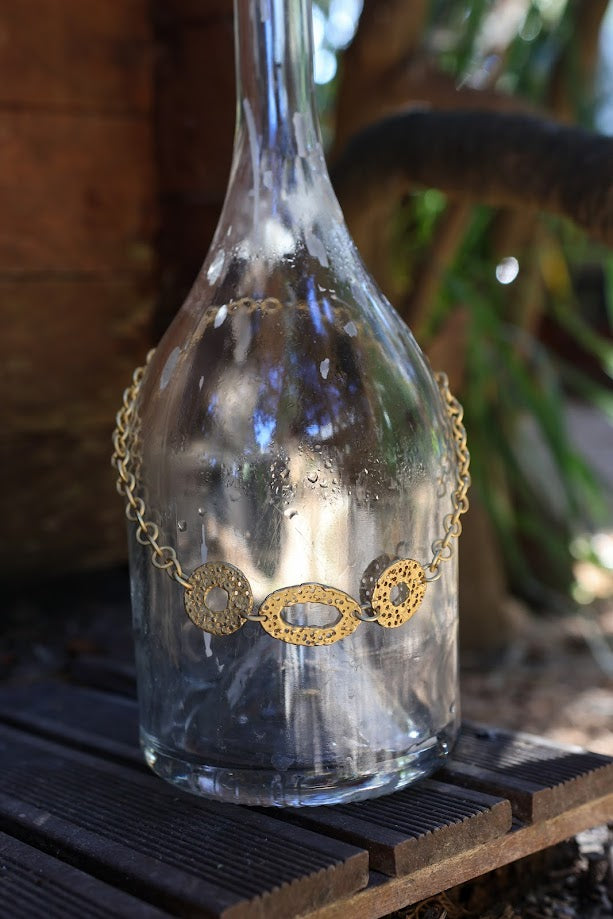 Colar Choker de corrente dourada, pendurado numa garrafa de vidro