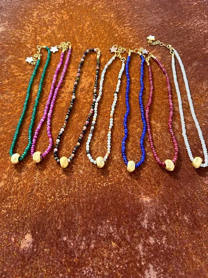 Colar Luísa de ágatas e aço dourado, várias cores lado a lado, sobre fundo cor de ferrugem