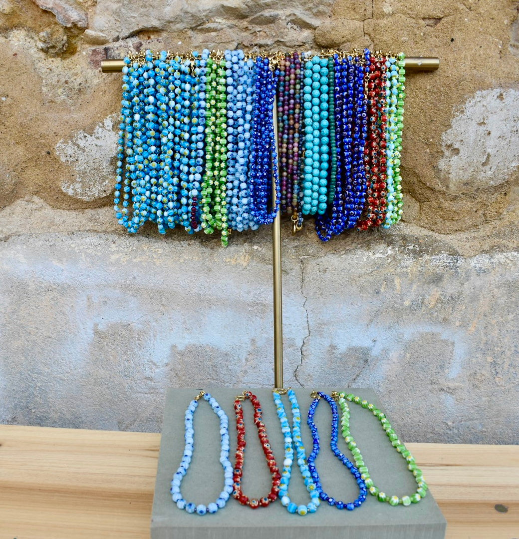 Colar Millefiori de vidro, várias cores num expositor, junto a uma parede de pedra