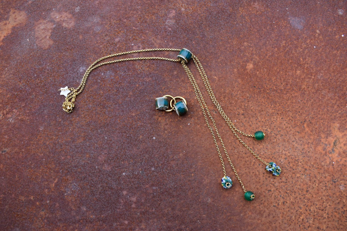 Colar Rain de aço dourado com pendentes, pormenor dos pendentes, sobre fundo cor de ferrugem