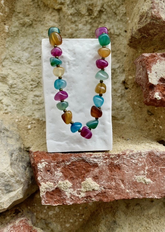 Colar Rainbow de ágatas, num expositor, junto a uma parede de pedra